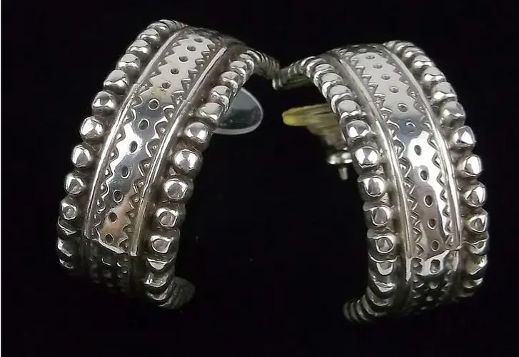 Pair of silver hoop earrings with intricate designs on a black background