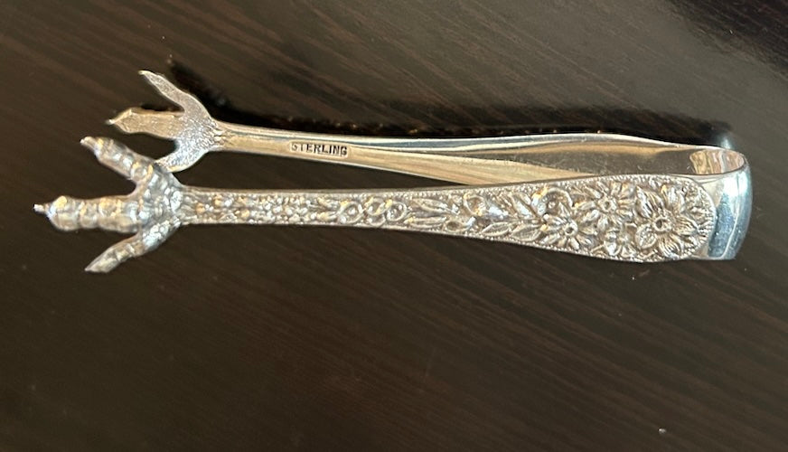 Antique sterling silver Bon Bon tongs with ornate repousse floral design and figural claws, perfect for serving treats.